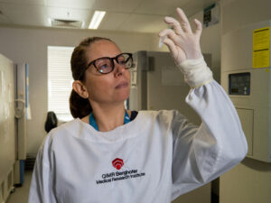 Female scientist in white lab coat in a laboratory looking closely at a small vial she is holding up